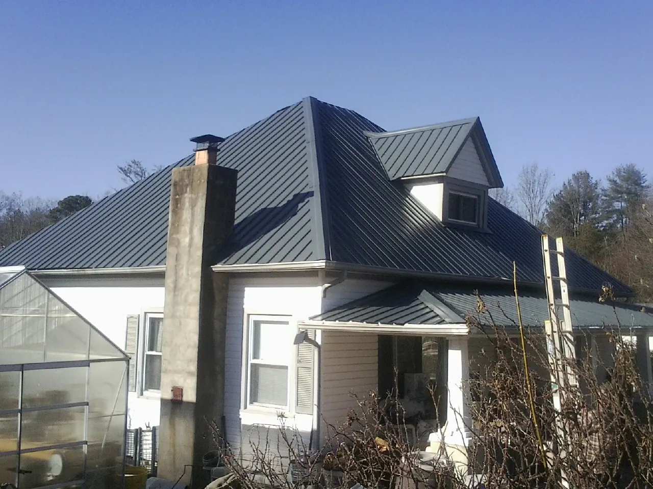 Dark blue standing seam metal roof on a white farmhouse with dormer — Slate & Tile Roof Repair by Roofing Brothers in Wilkinson
