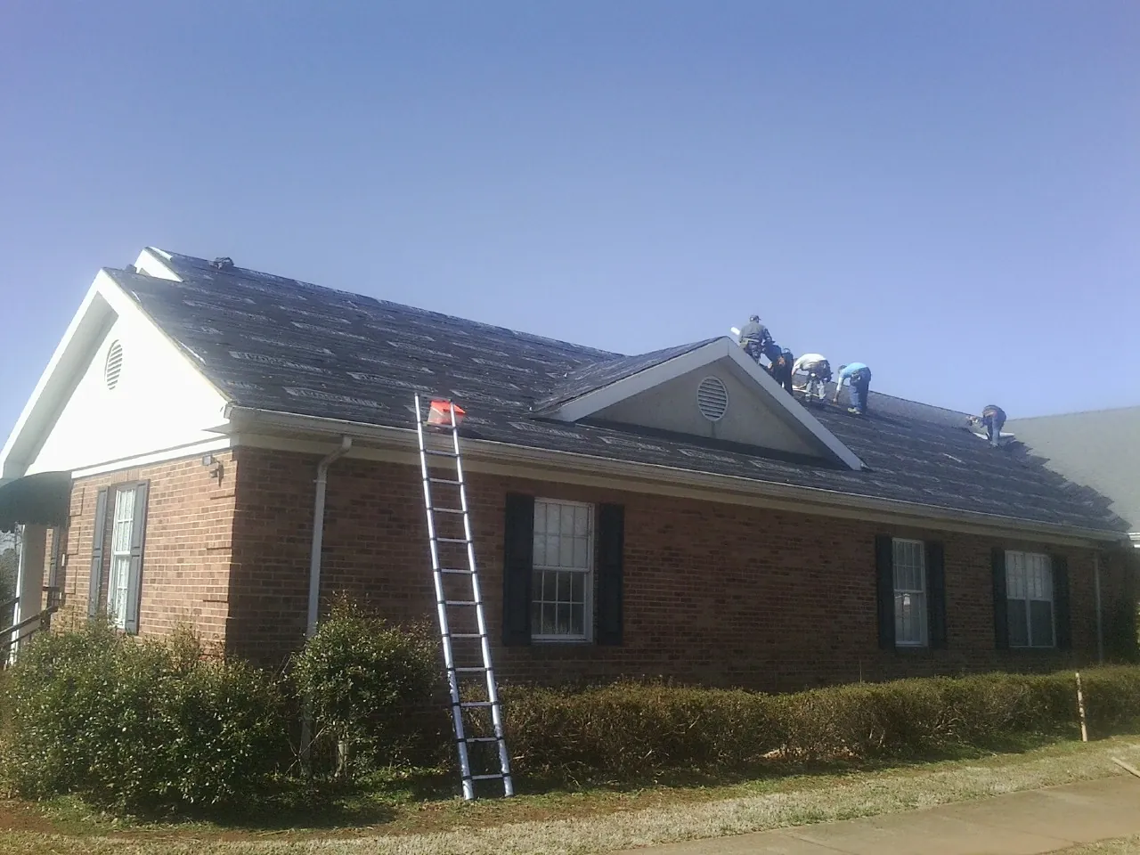 Crew tearing shingles off a brick ranch roof with a ladder set — Metal Roof Repair work by our crew in Wilkinson