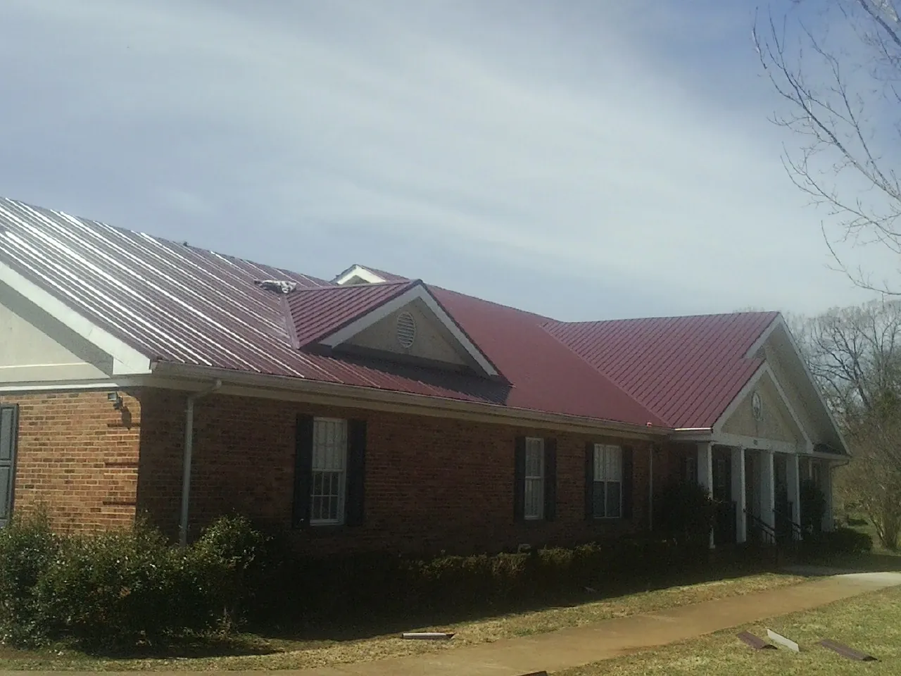 Red metal roof with gabled entries on a long brick building, from a Hail Damage Roof Repair job in Wilkinson