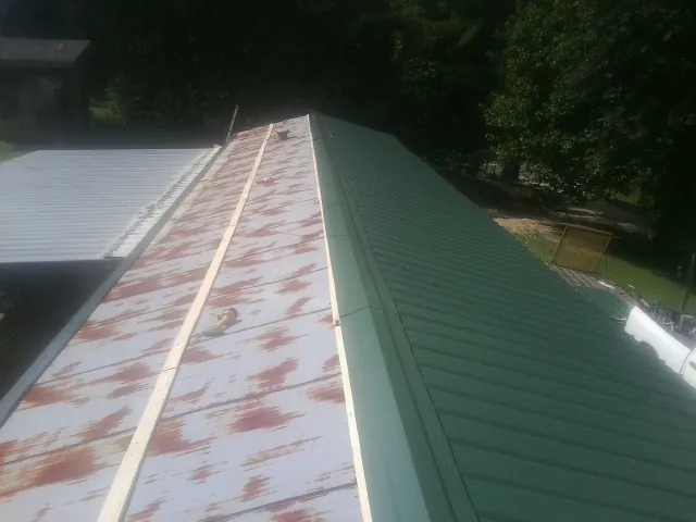 Old rusted panels beside newly installed green metal roofing — Wind Damage Roof Repair by Roofing Brothers in Wilkinson