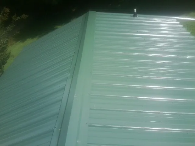 New green metal panels meeting at the ridge of a roof — Flat Roof Repair work by our crew in Wilkinson