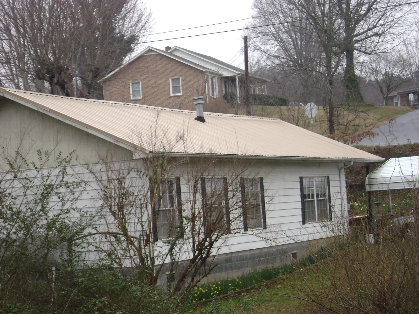 Tan metal roof on a white sided house set into a hillside — Commercial Roofing by Roofing Brothers in Wilkinson