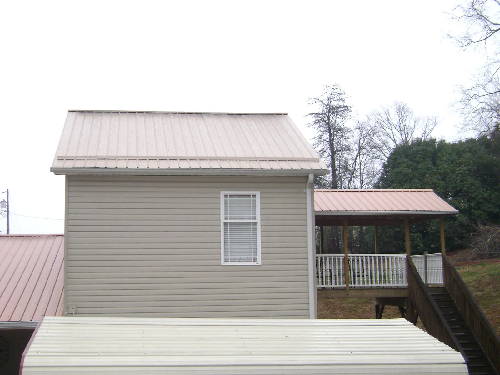 Tan metal roofs on a two story addition and attached porch, from a Roof Replacement job in Wilkinson