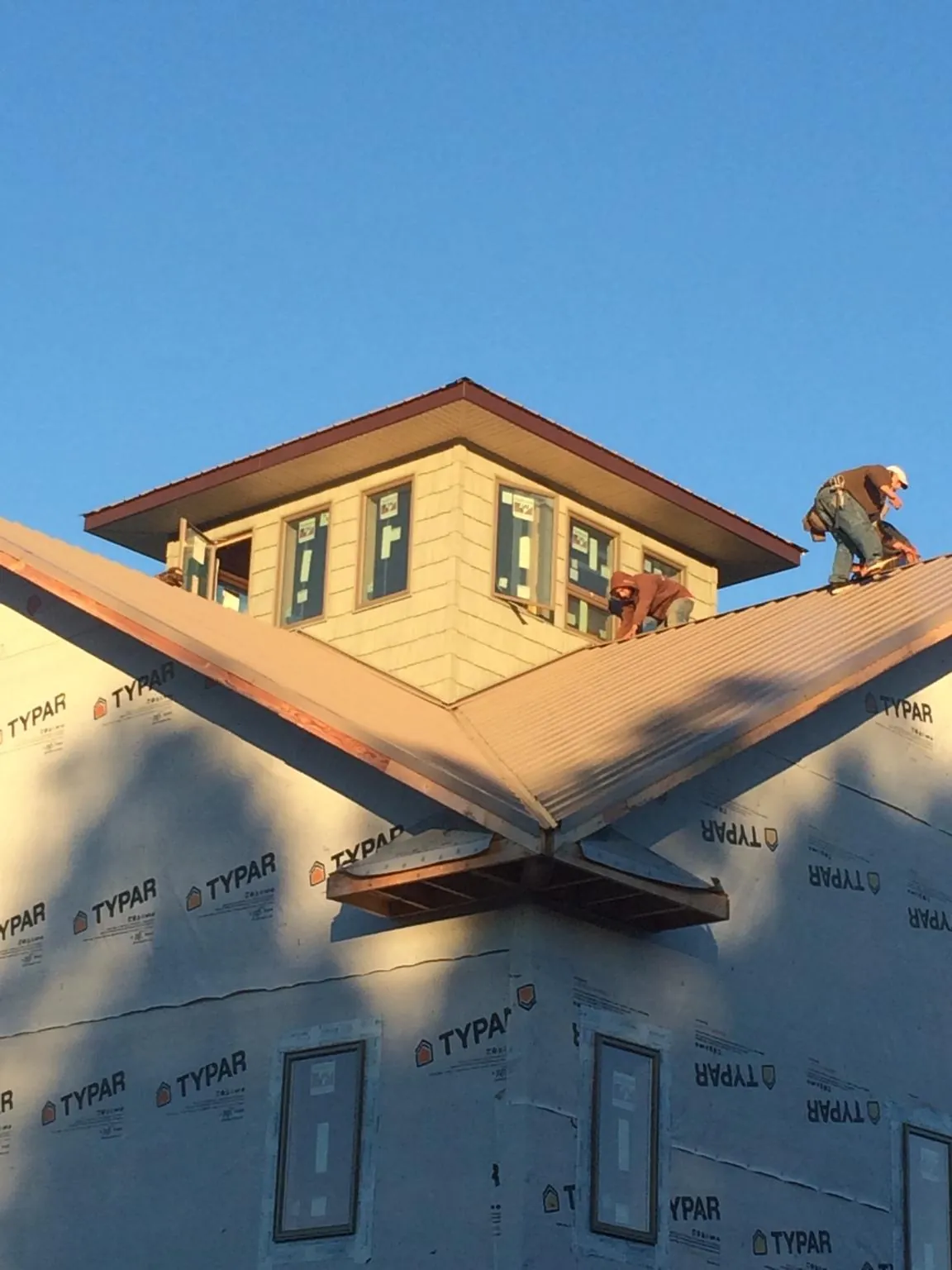Roofers working around a rooftop cupola on a new metal roof at sunset — Roof Waterproofing in Wilkinson by Roofing Brothers